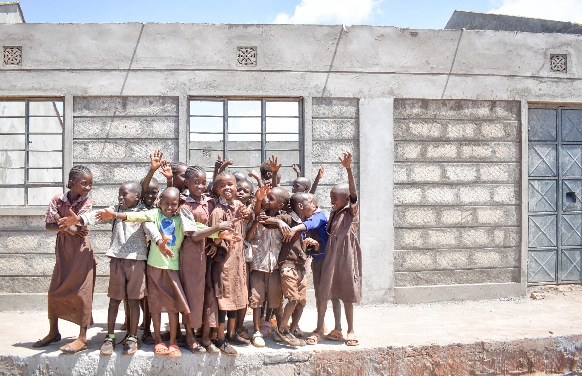 Children waving outside a school built with August Berg and the Human Practice Foundation