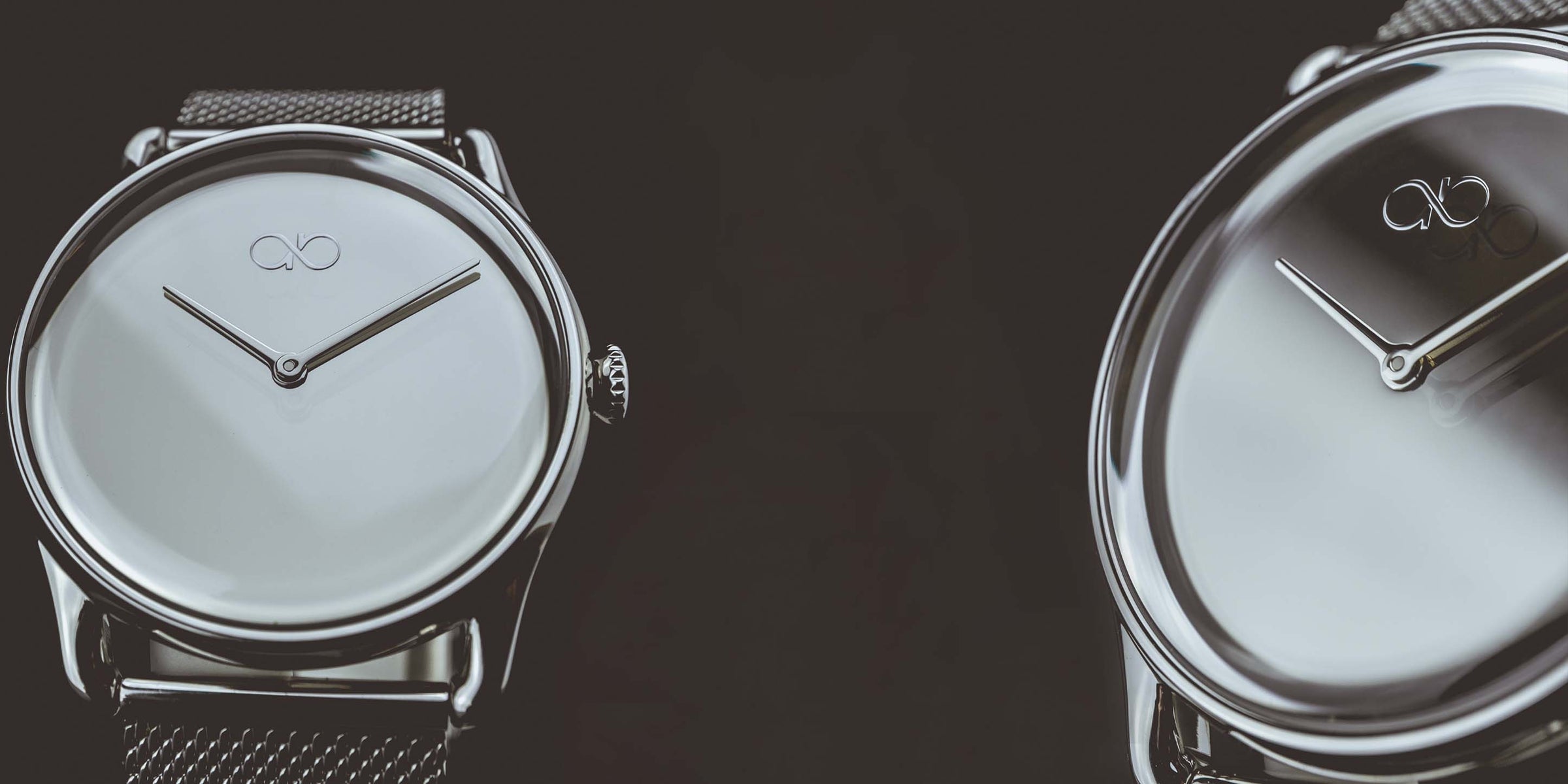 Two August Berg watches facing each other on a dark surface